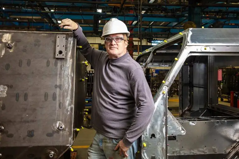 Happy Oshkosh Defense employee standing by an assembly line.