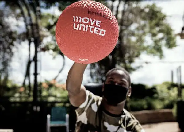 Boy holding a red ball with the Move United logo.