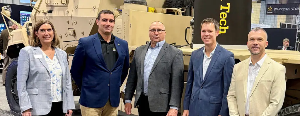 Janet Keech and Steve Herrick of Oshkosh Defense stand with Henry Schmidt, Kevin Meyers, and Jeff Naber of Michigan Technological University in front of an FMTV A2 tactical vehicle, marking the partnership to advance the Vehicle Integrated Power Kit (VIPK)